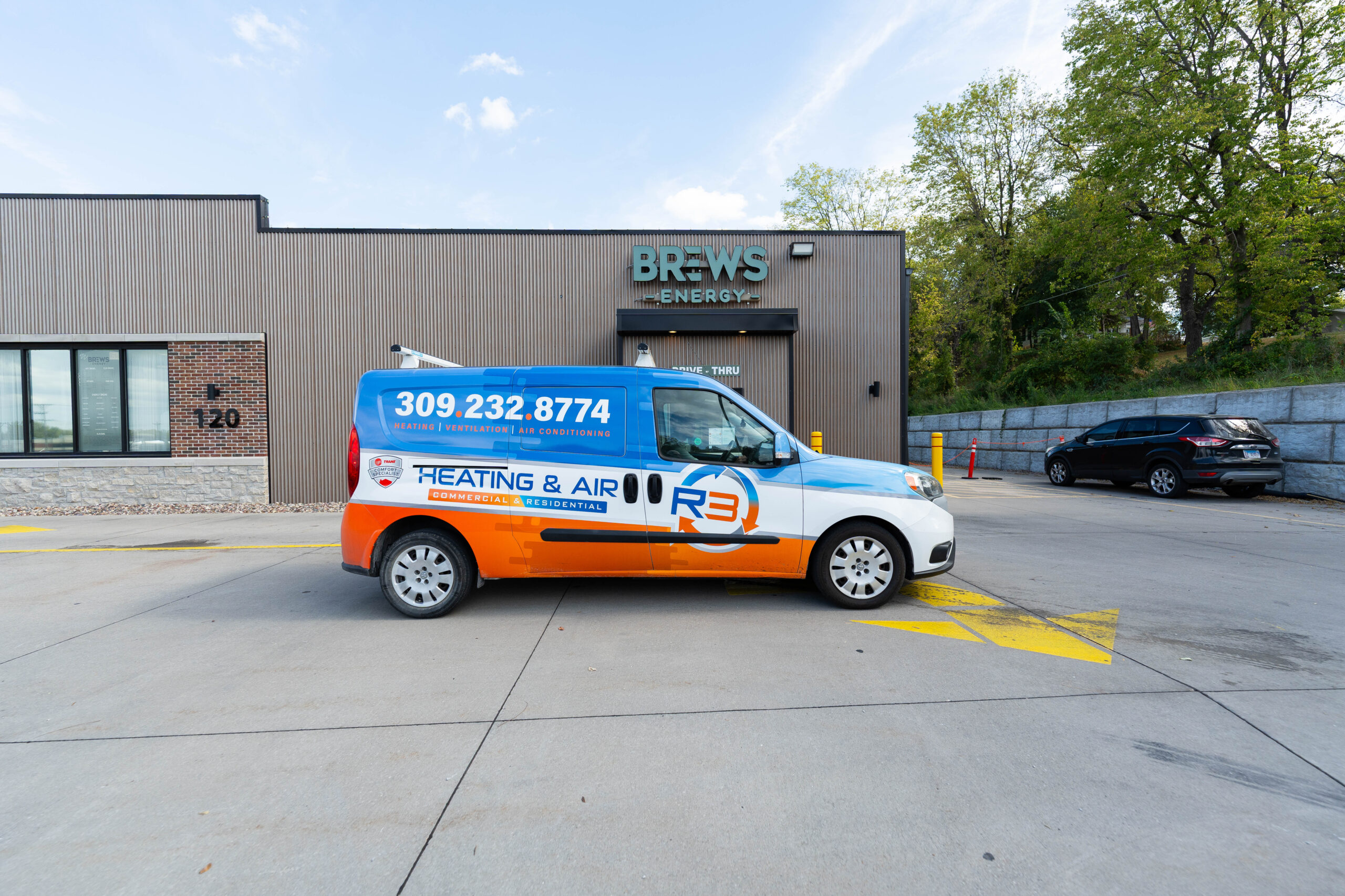 R3 Heating & Air technician standing by an R3 service truck outside a residential home in Iowa, ready to provide HVAC maintenance and repair.